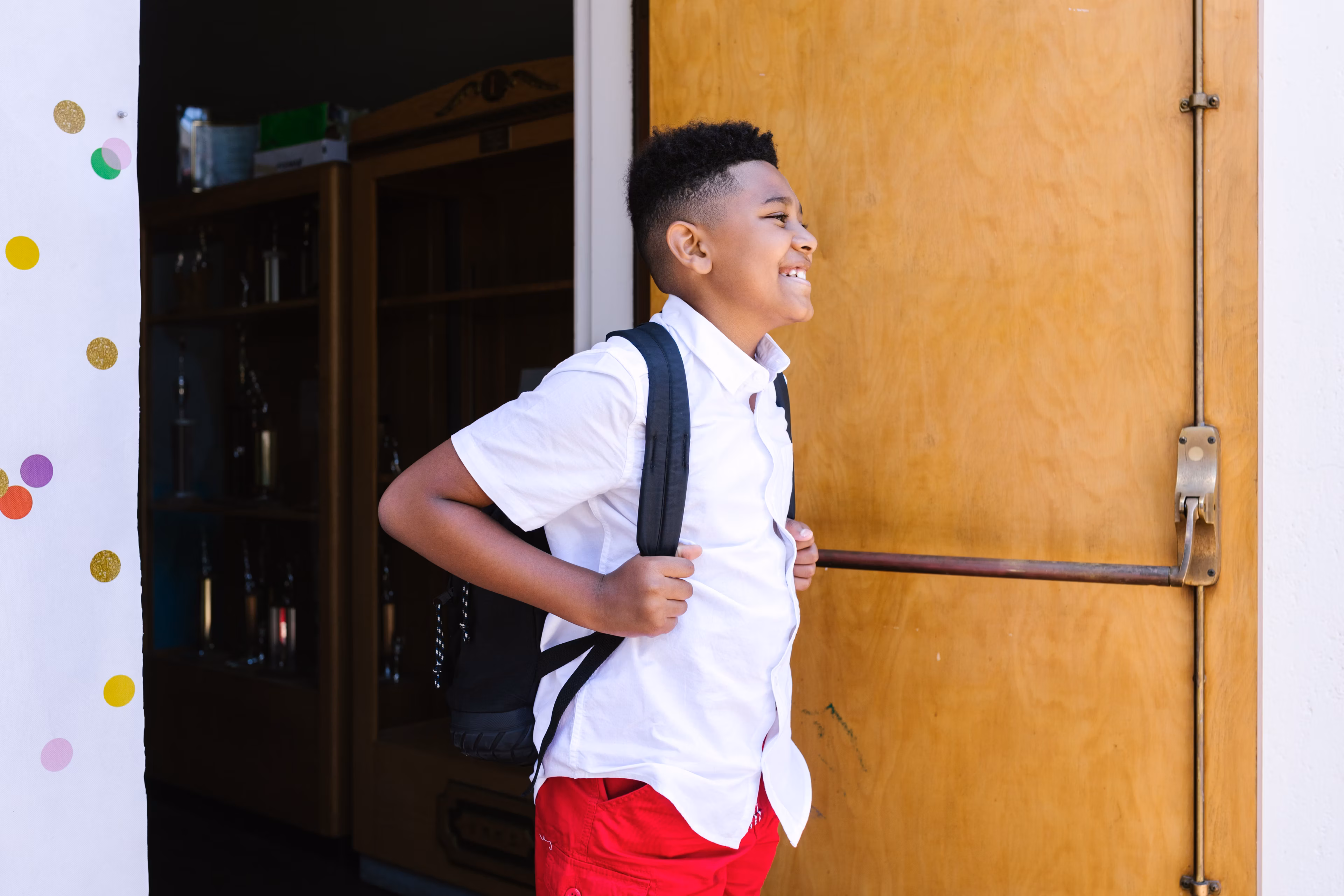 Smiling boy with a backpack arriving happily at school